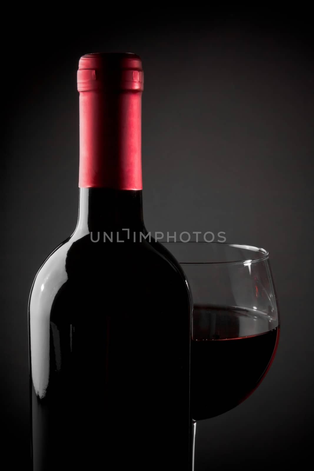 red wine glass near bottle on grey background