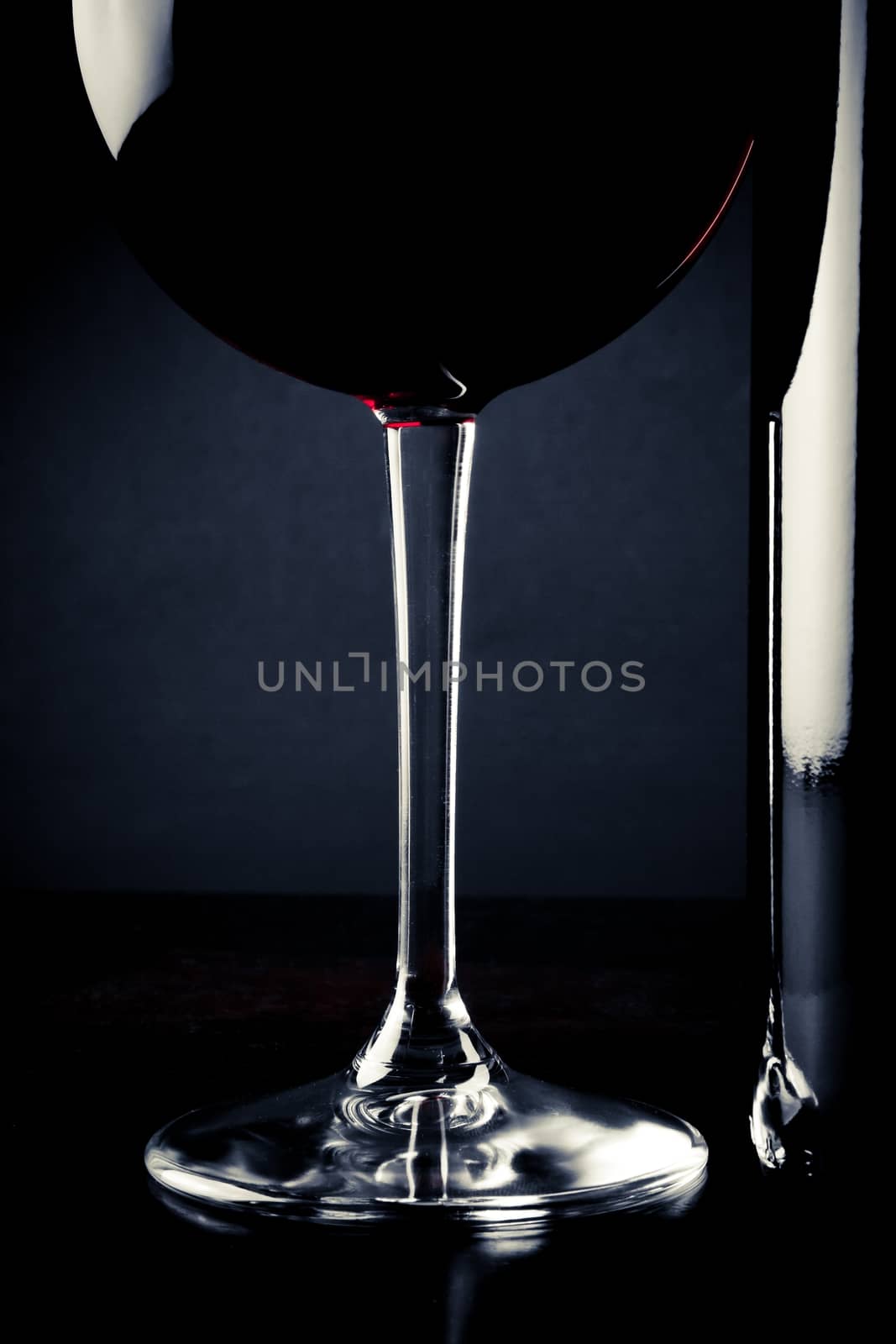 detail of red wine glass near bottle on wood table
