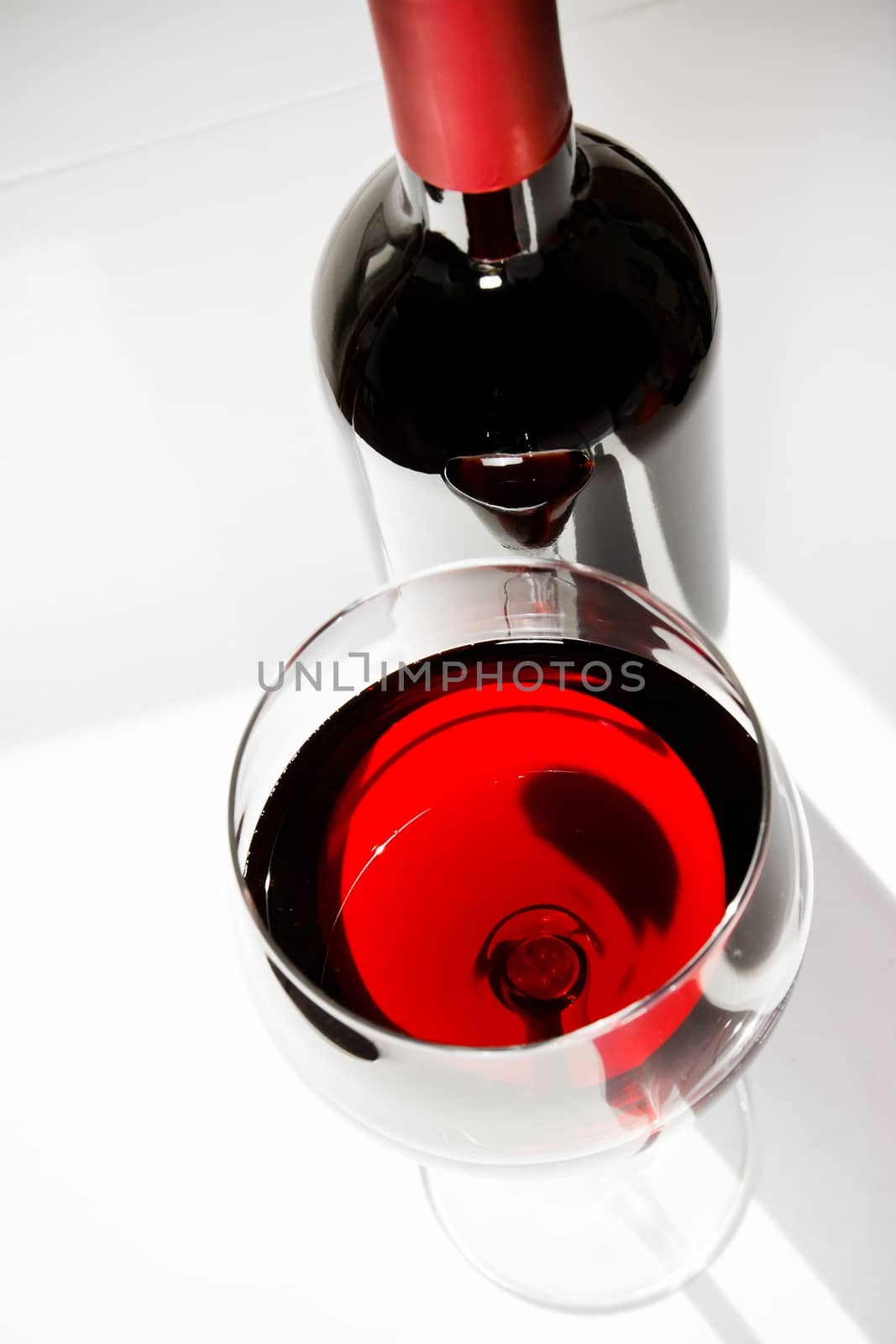 red wine glass near a bottle under daily light on white table