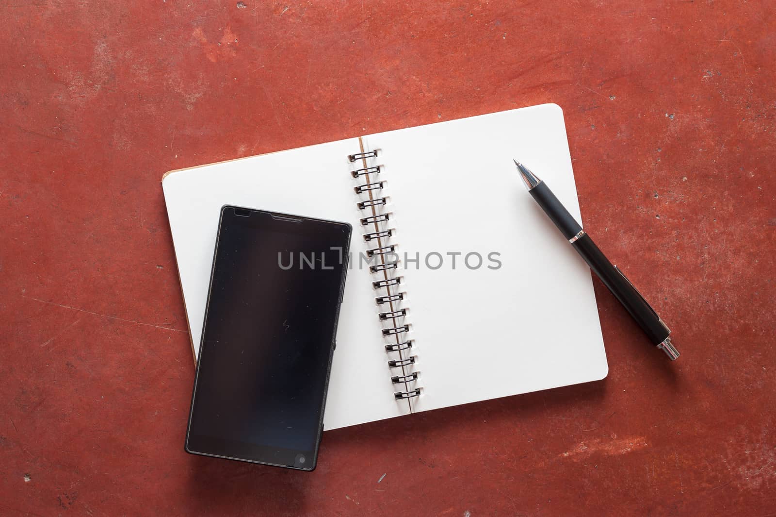 Opened notepad with pen and black smart phone on rustic cement background with low key scene.