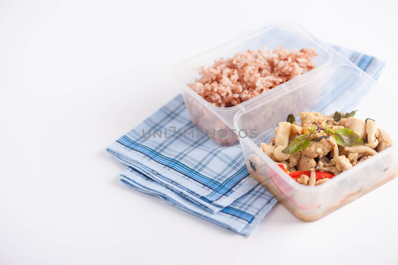 Stir freid basil with chicken breast and Termitomyces cooked by clean food concept with brown rice in lunch box on white table