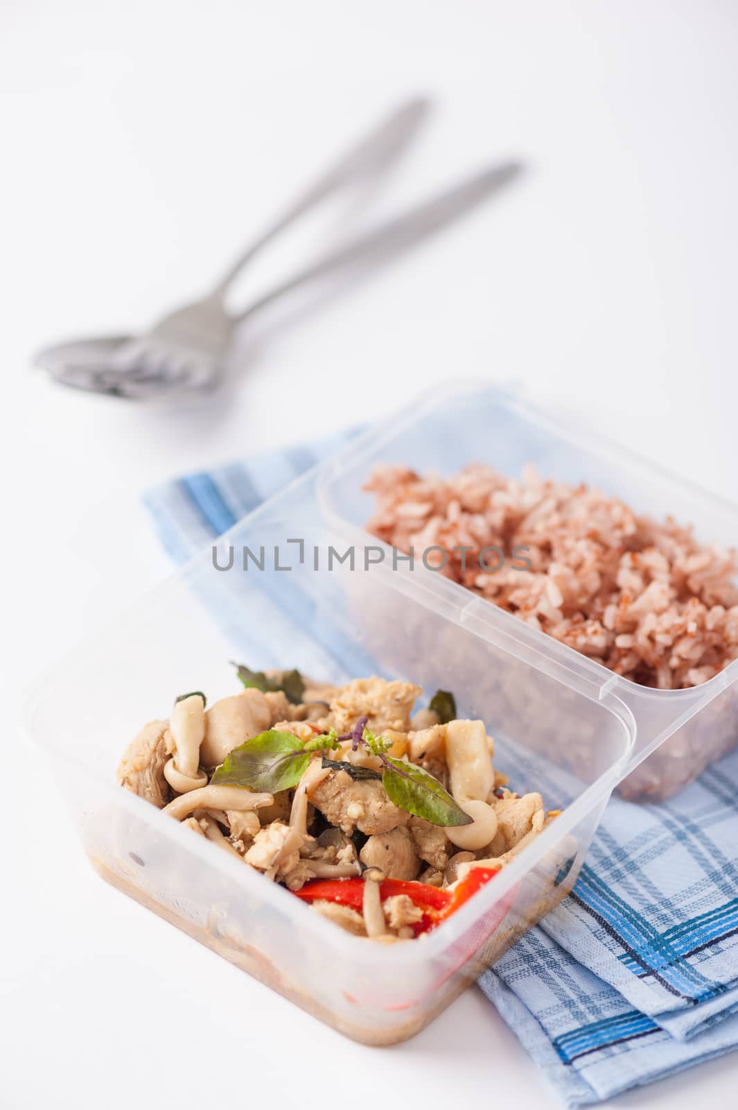 Stir freid basil with chicken breast and Termitomyces cooked by clean food concept with brown rice in lunch box on white table