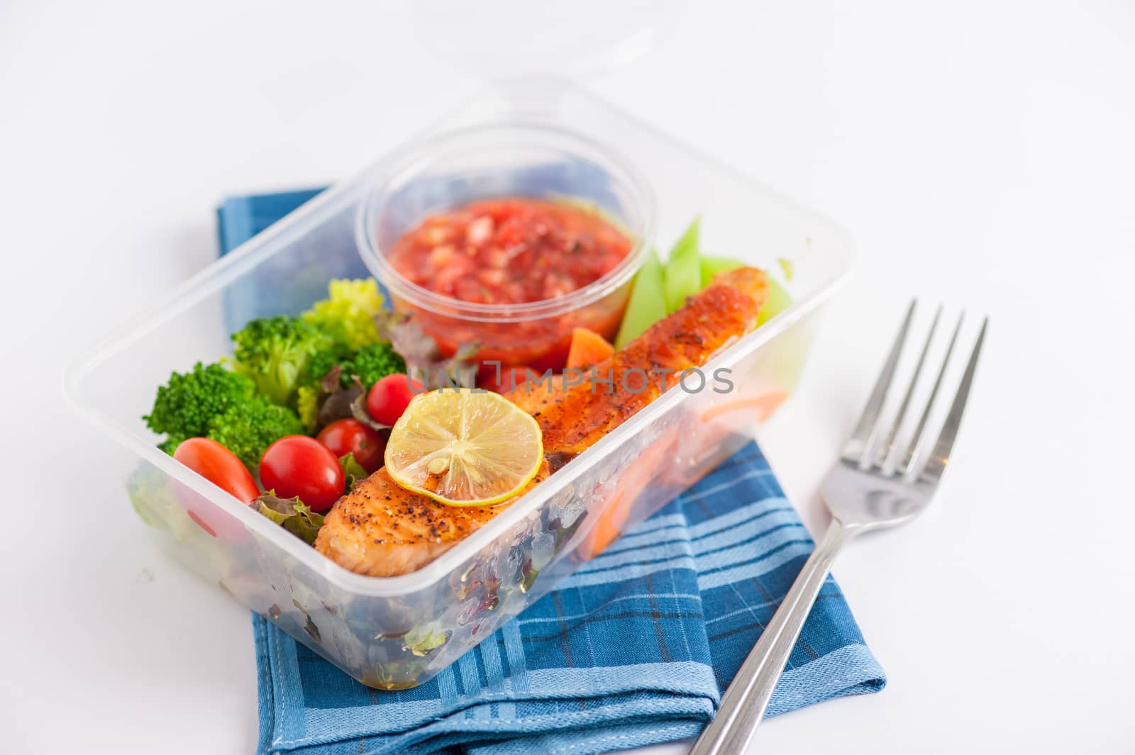 Grilled salmon with tomato salsa and salad cooked by clean food concept in lunch box on white table