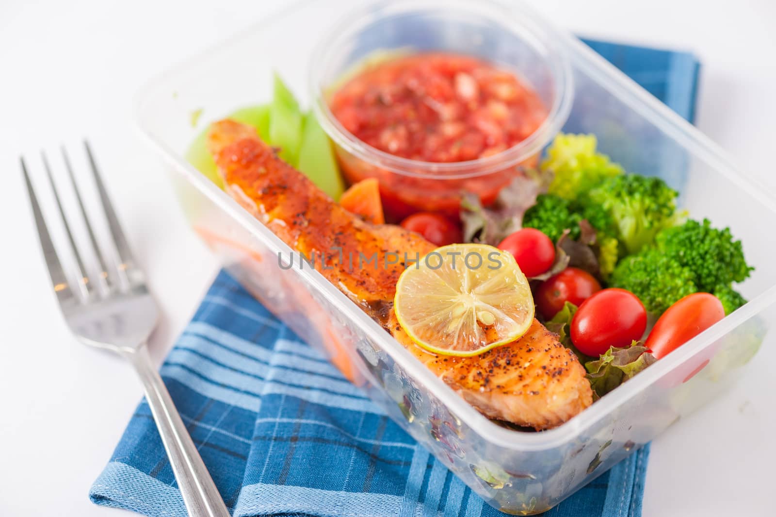 Grilled salmon with tomato salsa and salad cooked by clean food concept in lunch box on white table