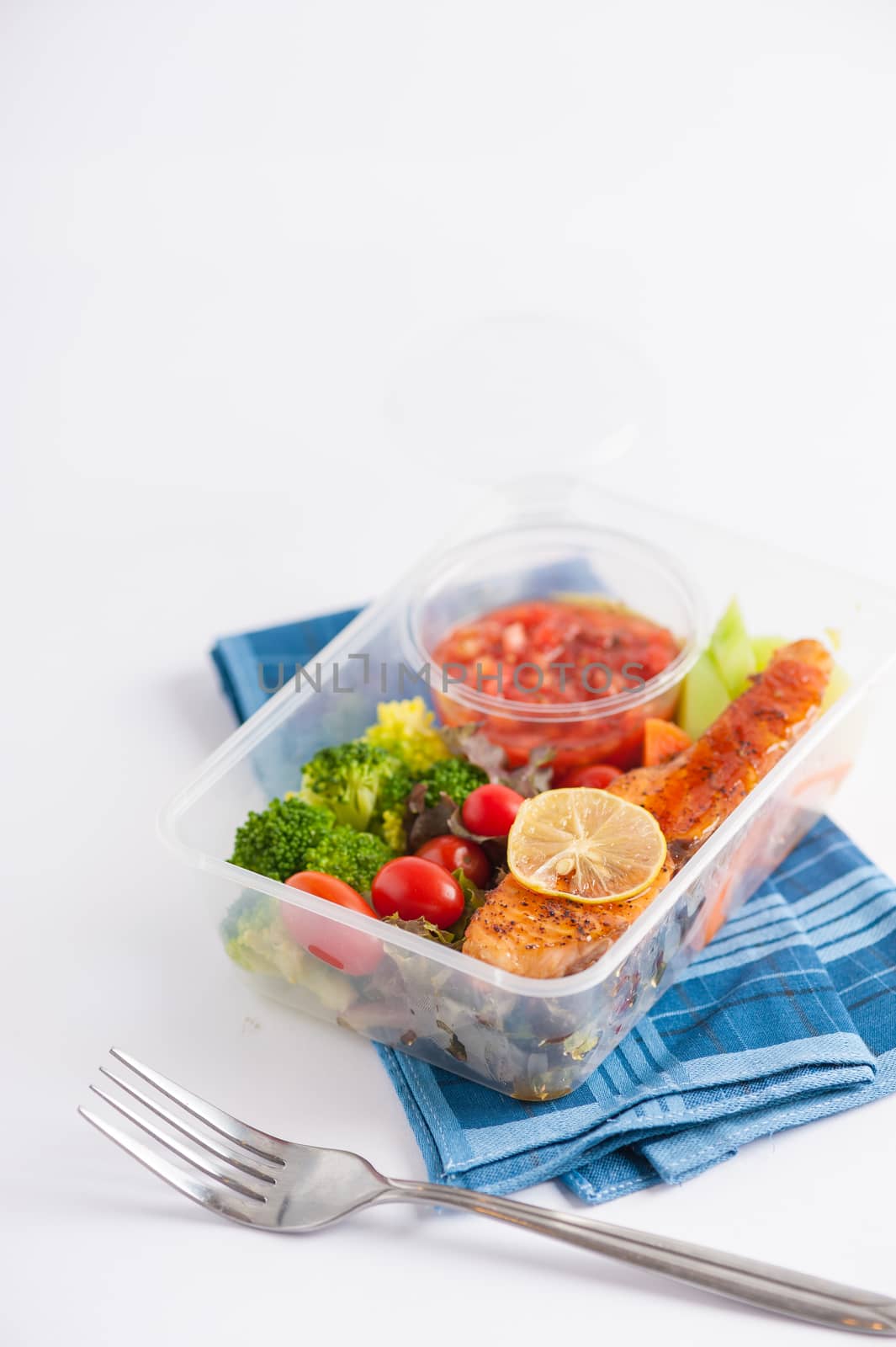Grilled salmon with tomato salsa and salad cooked by clean food concept in lunch box on white table