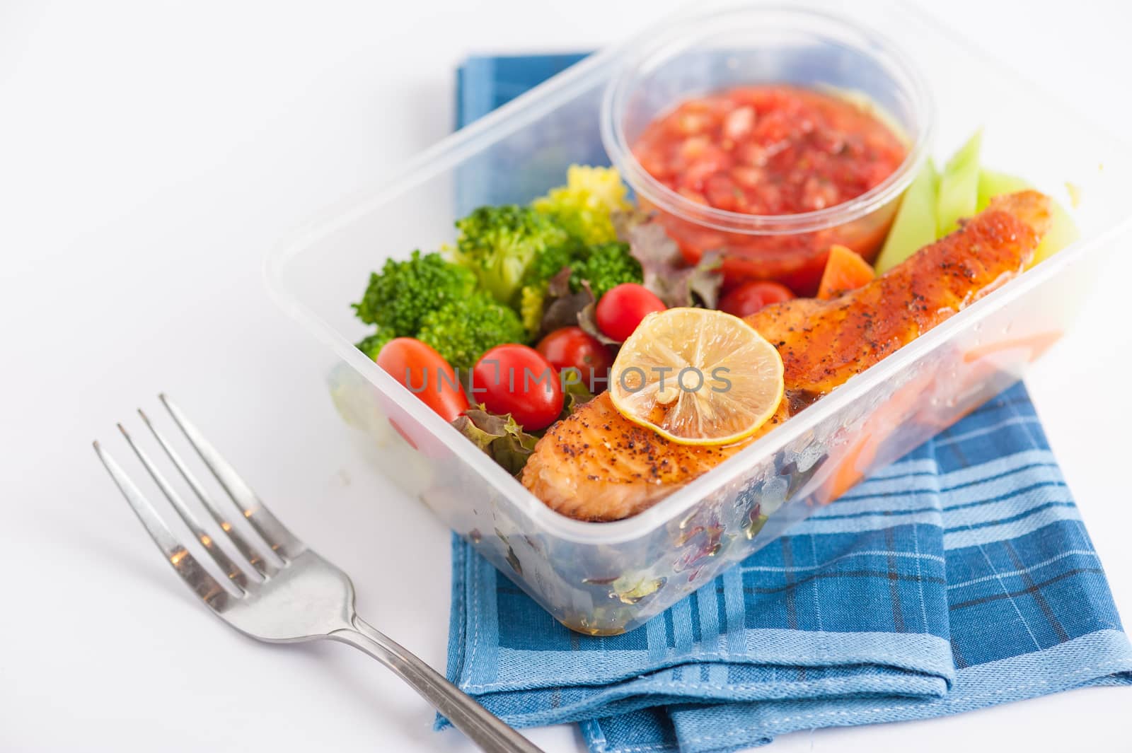 Grilled salmon with tomato salsa and salad cooked by clean food concept in lunch box on white table