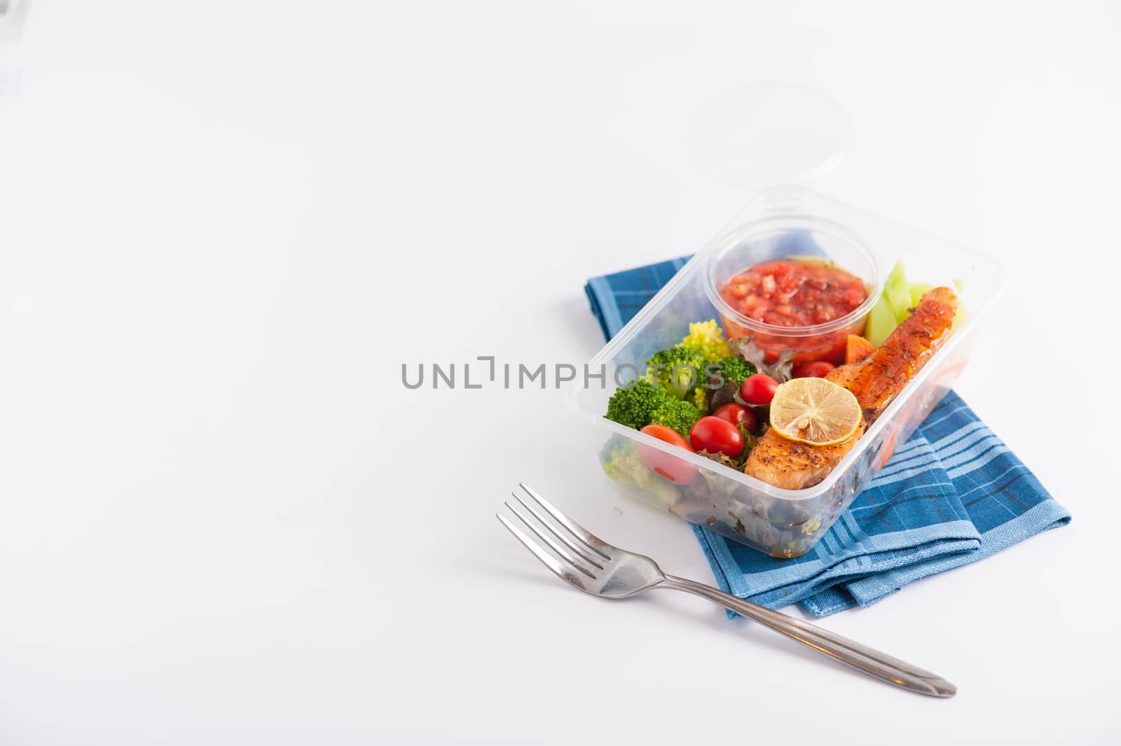 Grilled salmon with tomato salsa and salad cooked by clean food concept in lunch box on white table