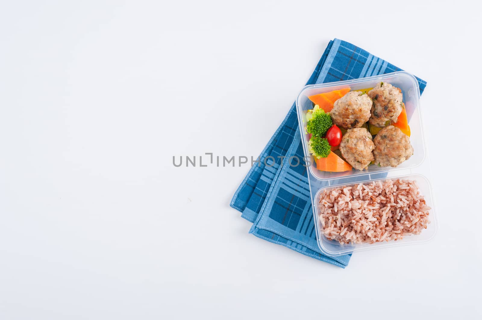 Thai style fried pork ball cooked by clean food concept with vegetables and brown rice in lunch box on white table