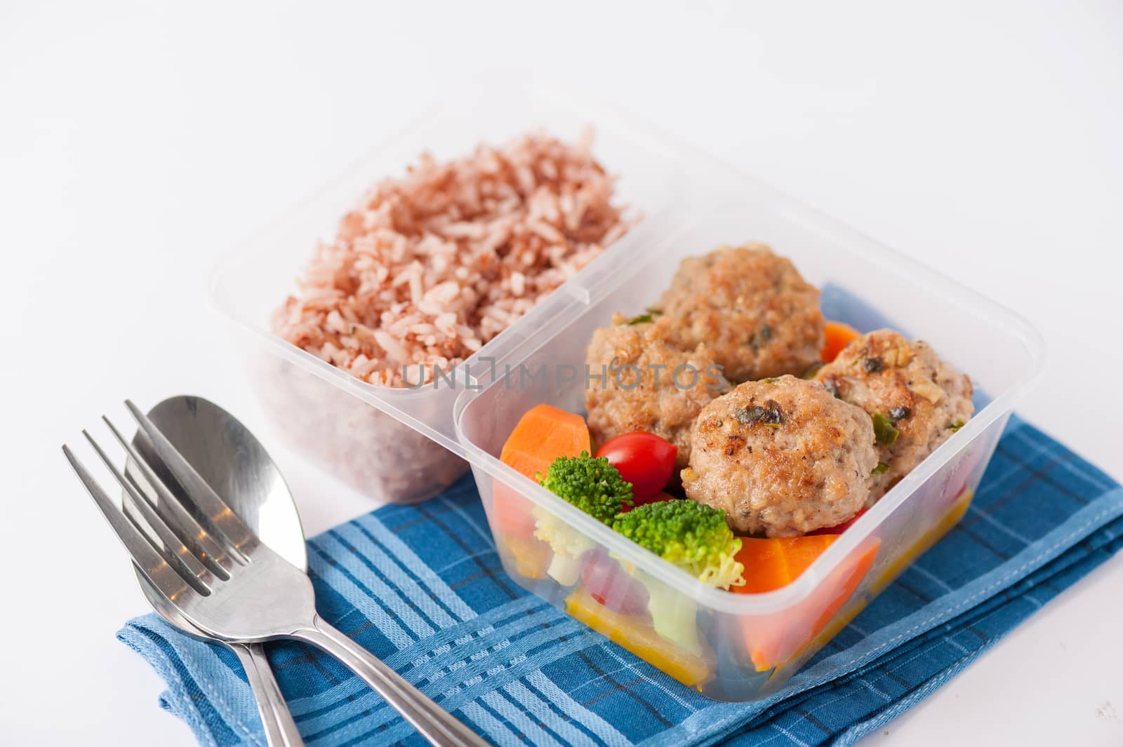 Thai style fried pork ball cooked by clean food concept with vegetables and brown rice in lunch box on white table