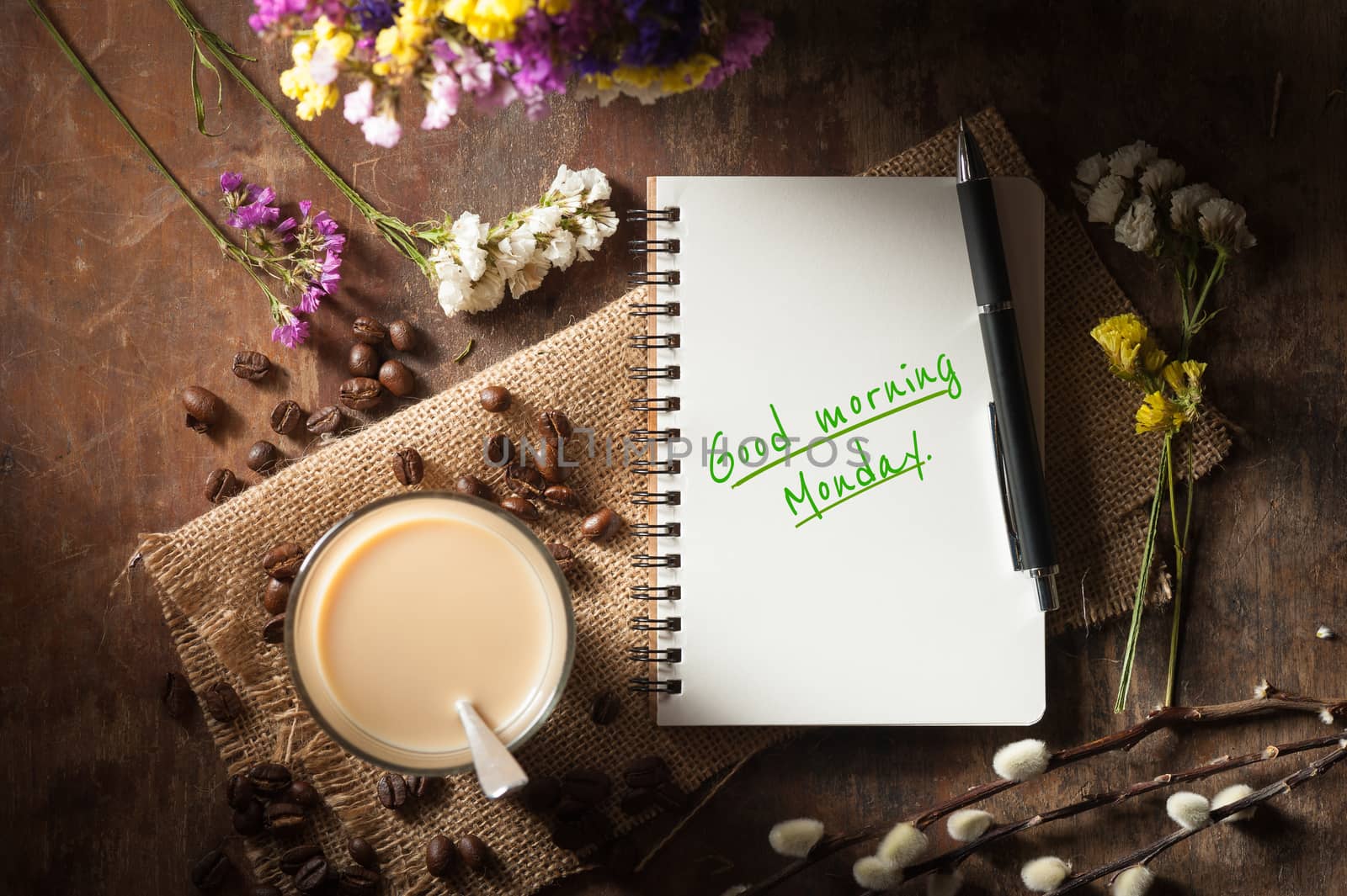 "Good morning monday" is written on Notepad with pen, a glass of Thai tea and bits of red velvet cake on rustic wood background with low key scene