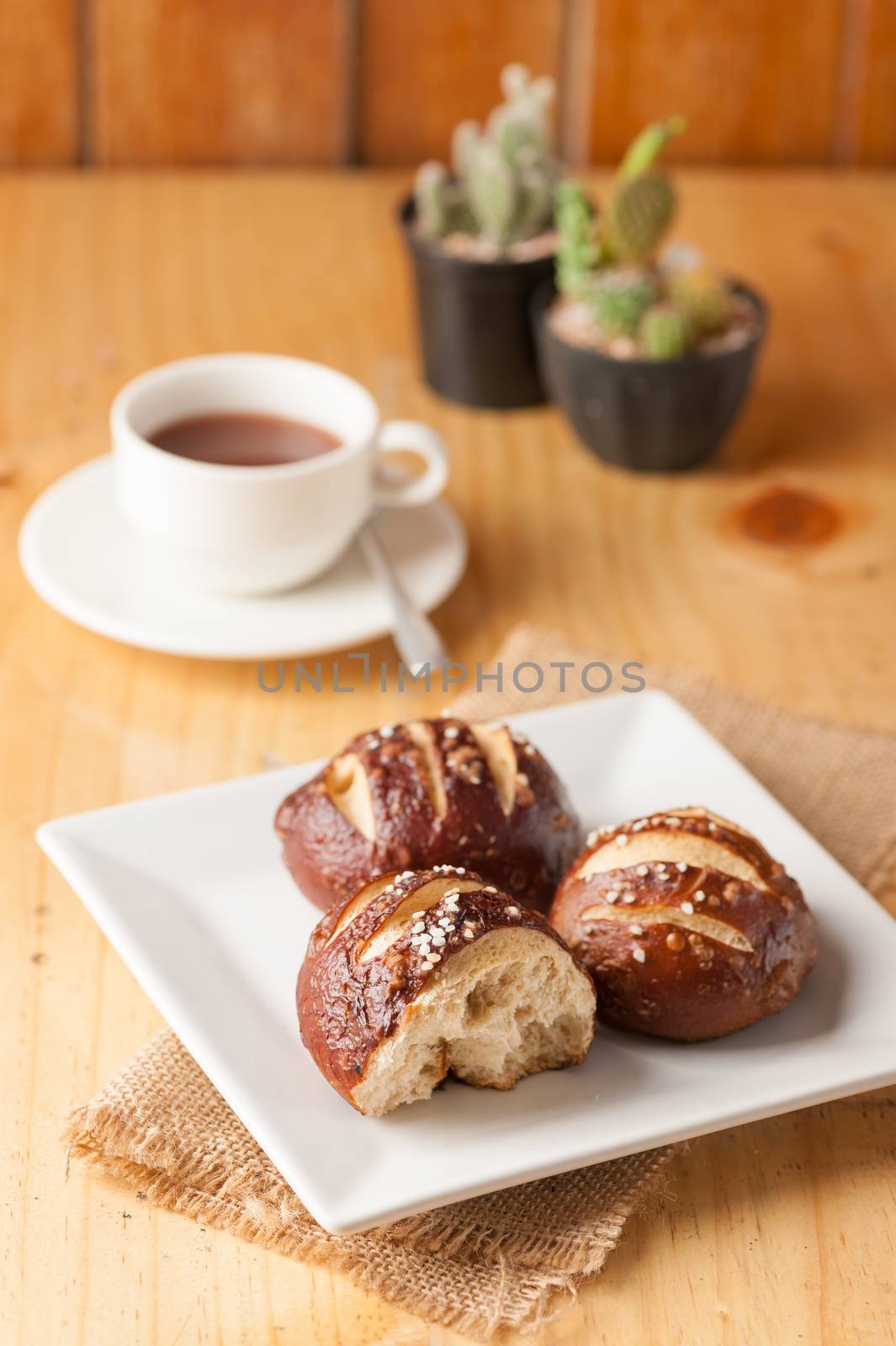 Freshly baked soft pretzel with generous sprinkling of coarse salt on white dish and a cup of hot chocolate in background