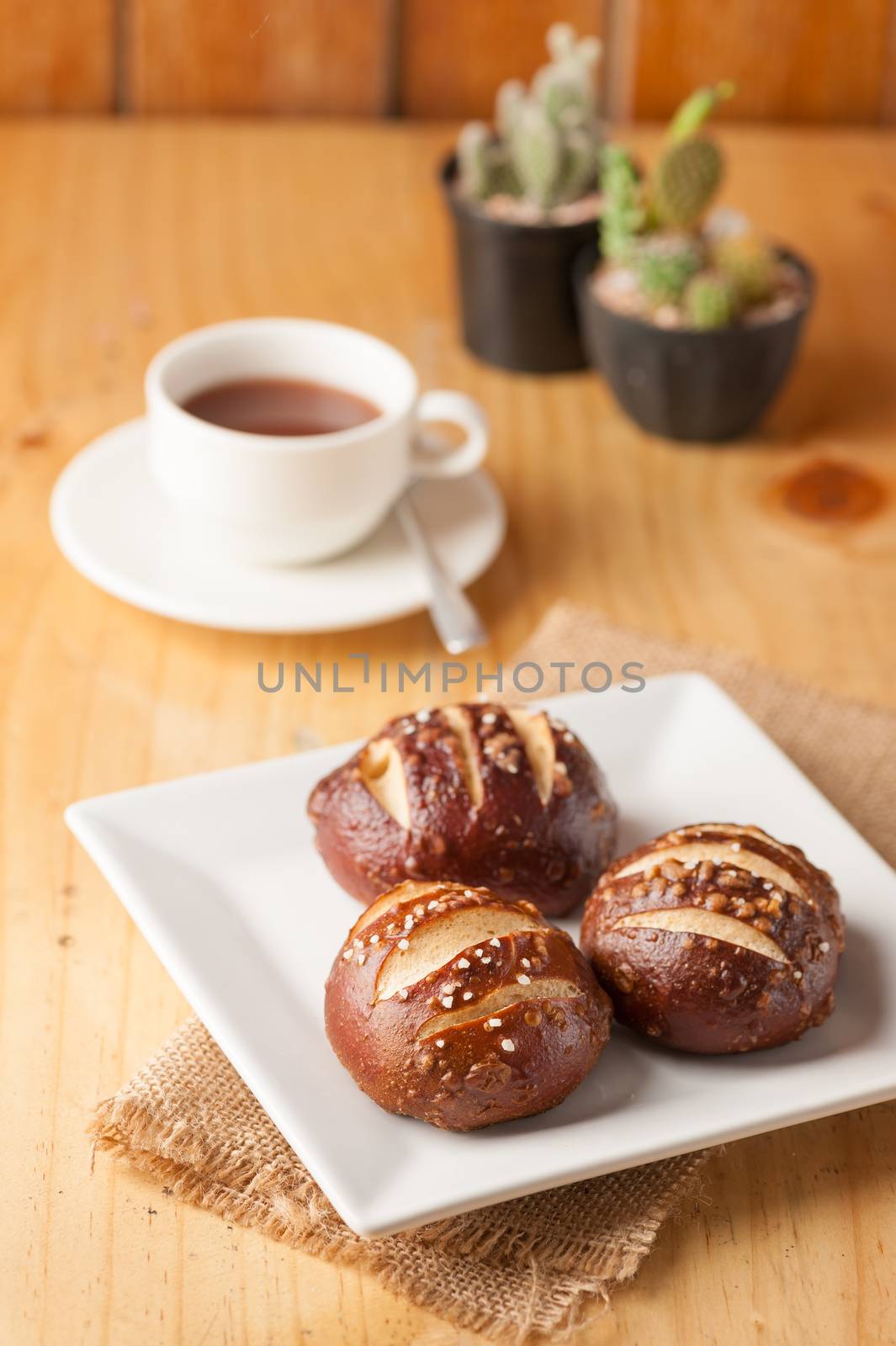 Freshly baked soft pretzel with generous sprinkling of coarse salt on white dish and a cup of hot chocolate in background