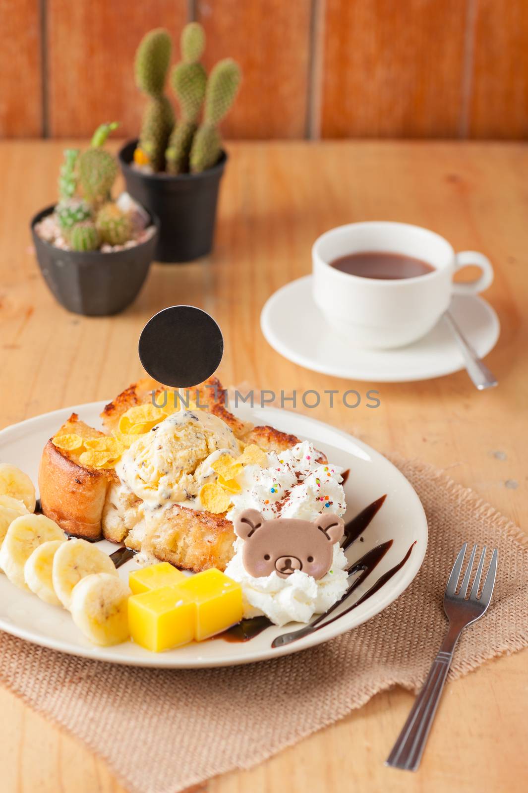 Honey toast with banana, whipped cream, chocolate chip ice cream, and mango jelly on white dish with black circle tag stab down on the ice cream in vintage scene