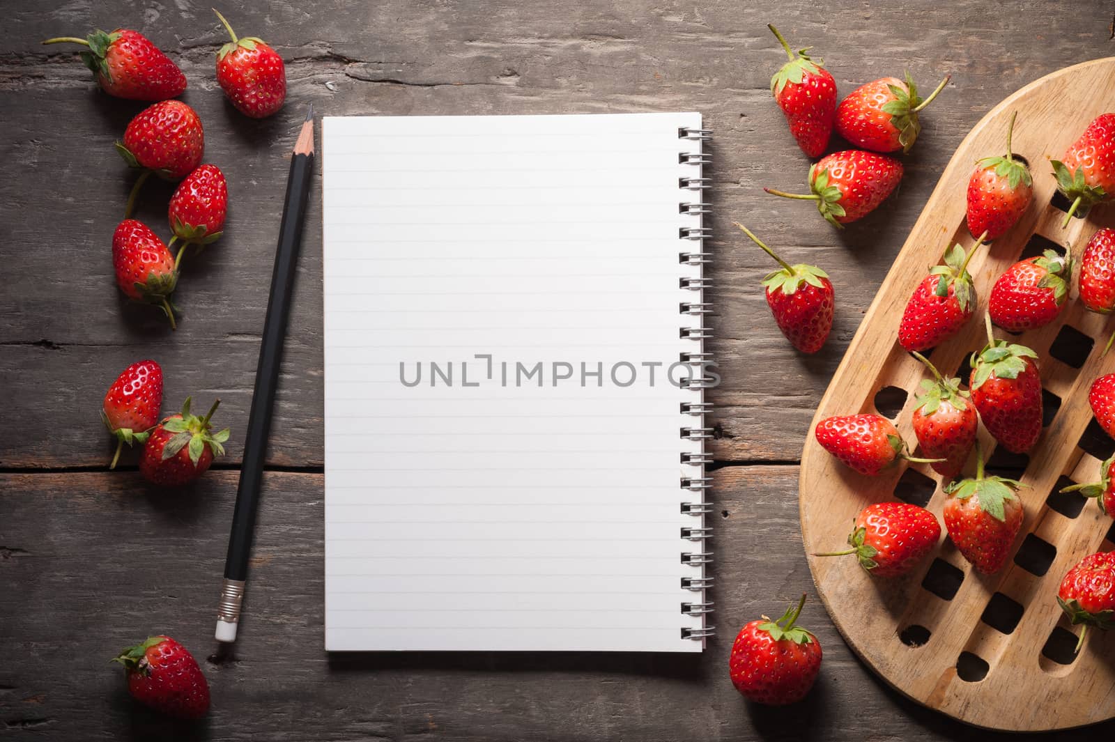 Strawberries and notebook on wood background in vintage style with low key scene.