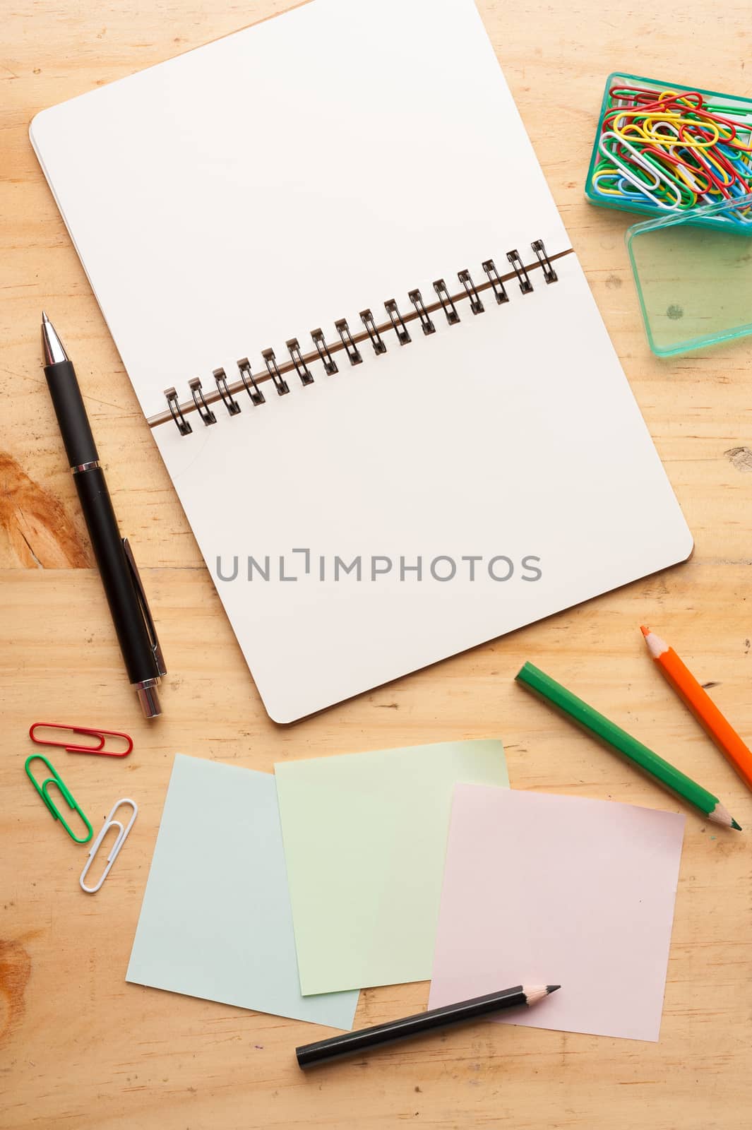 Notebook and sticky paper, paper clip, color pencil, and pen on wood table