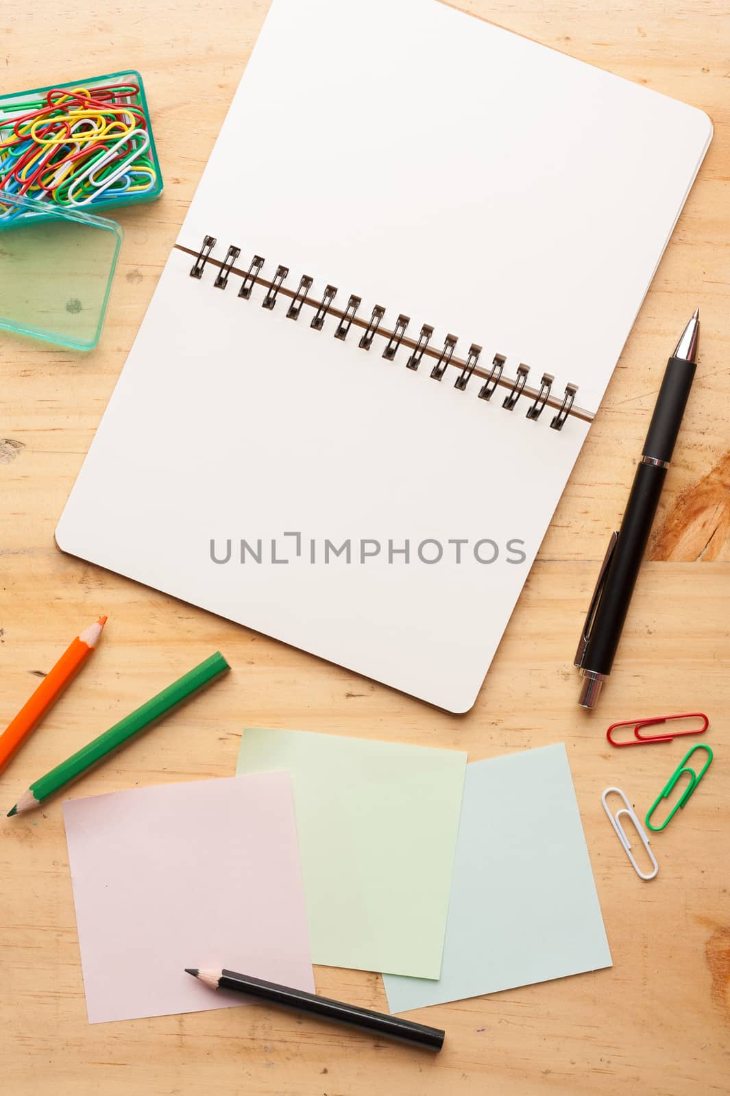 Notebook and sticky paper, paper clip, color pencil, and pen on wood table