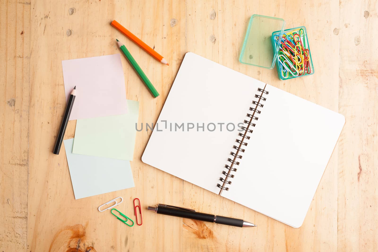 Notebook and sticky paper, paper clip, color pencil, and pen on wood table