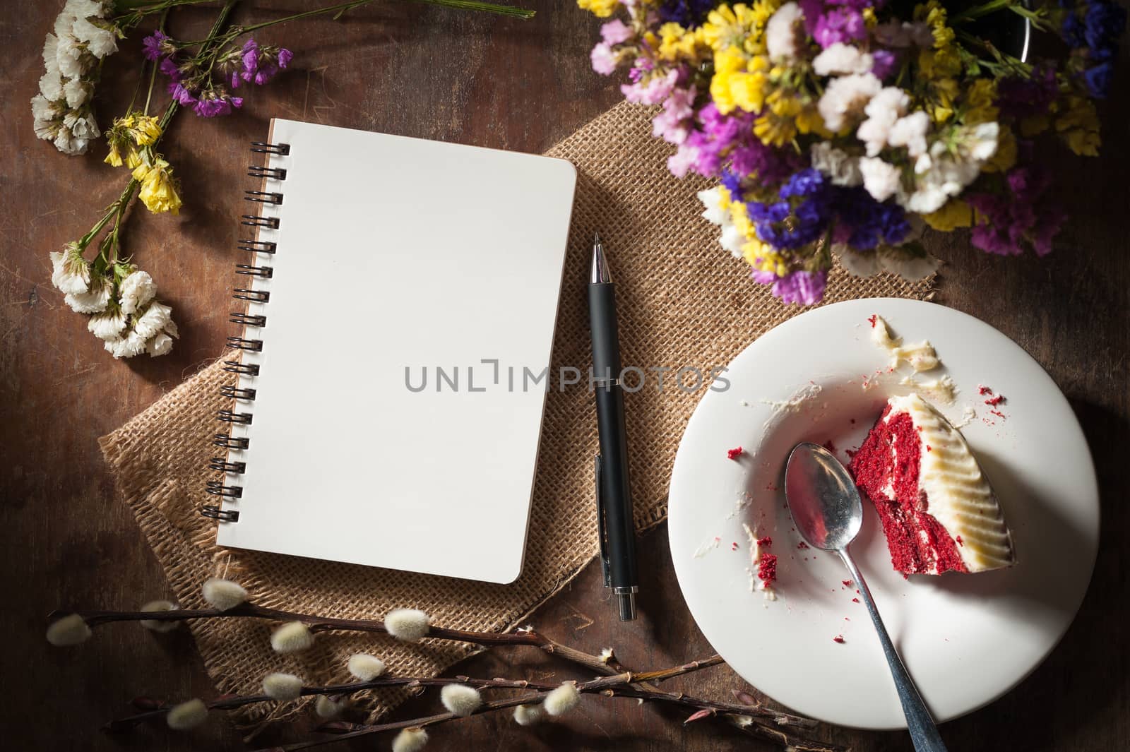 Small notepad with pen, pencil and bits of red velvet cake on rustic wood background with low key scene.