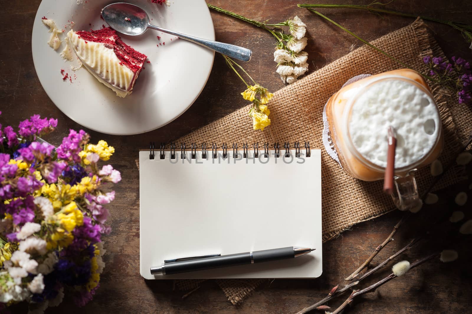 Notepad with pen, a glass of Thai tea and bits of red velvet cake on rustic wood background with low key scene