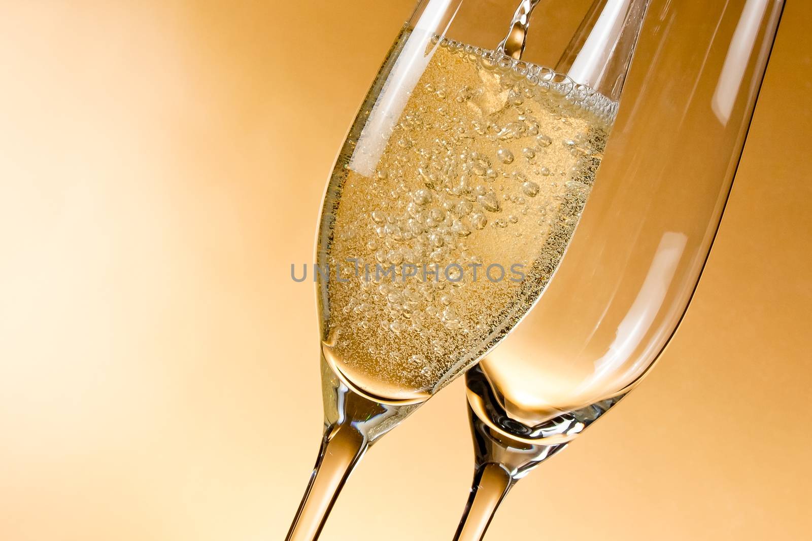 empty glasses of champagne and one being filled against golden background