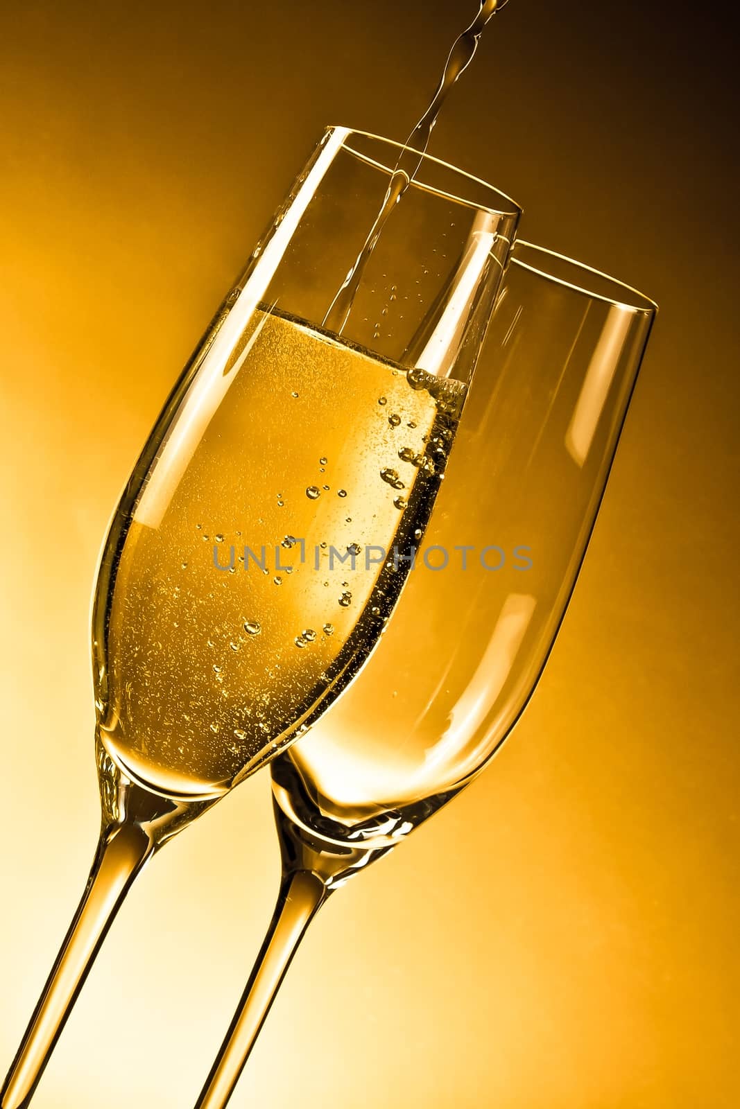 empty glasses of champagne and one being filled against golden background