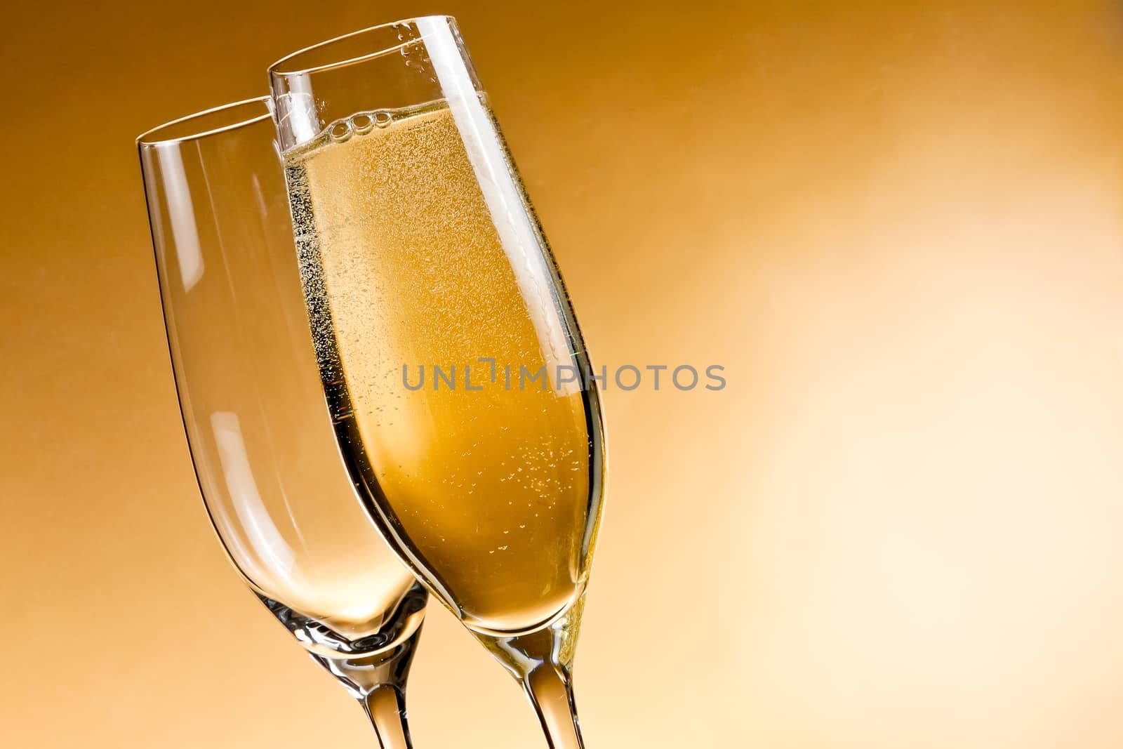 one empty glass of champagne and one filled on golden background