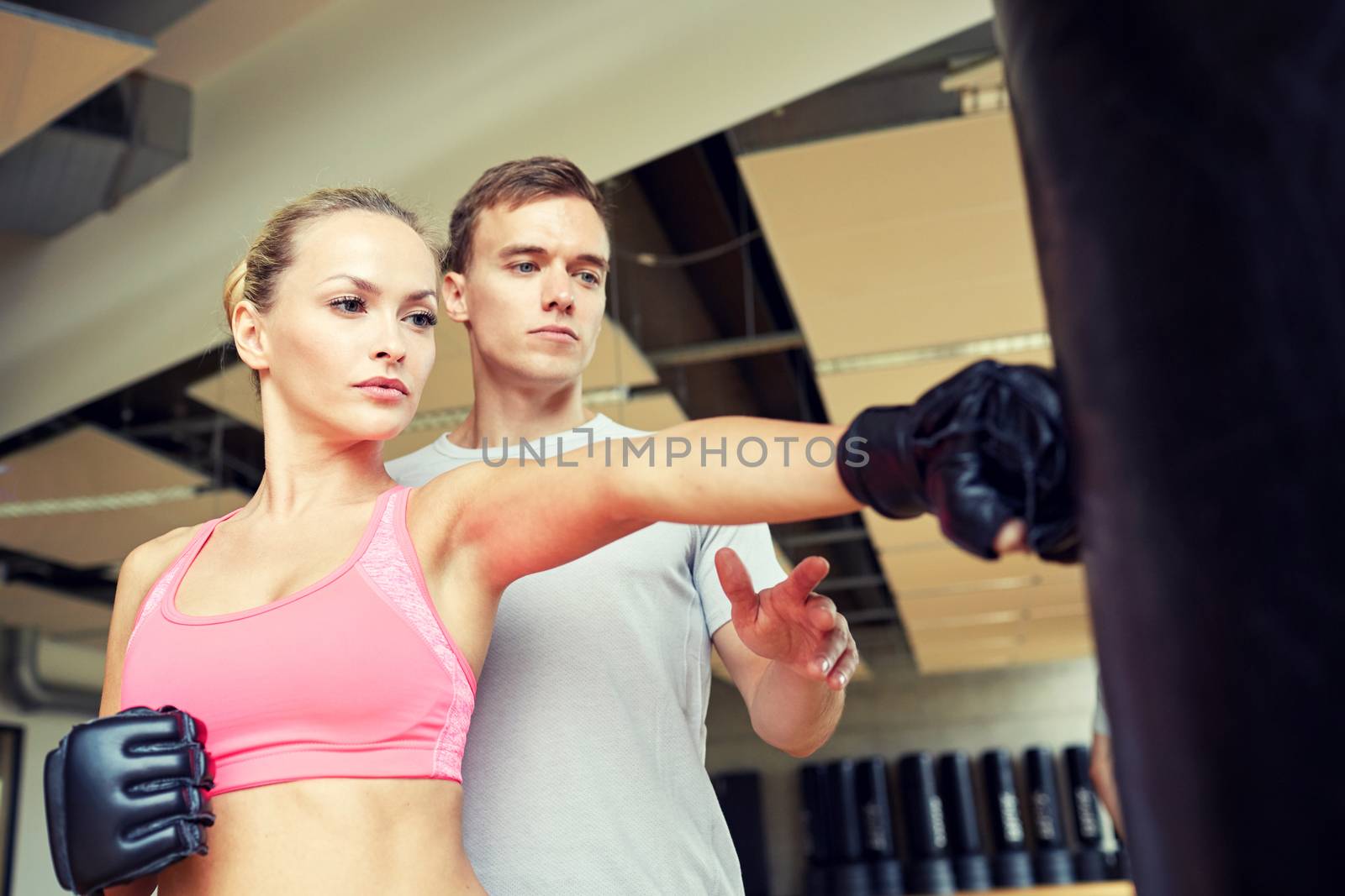 sport, fitness, lifestyle and people concept - woman with personal trainer boxing punching bag in gym