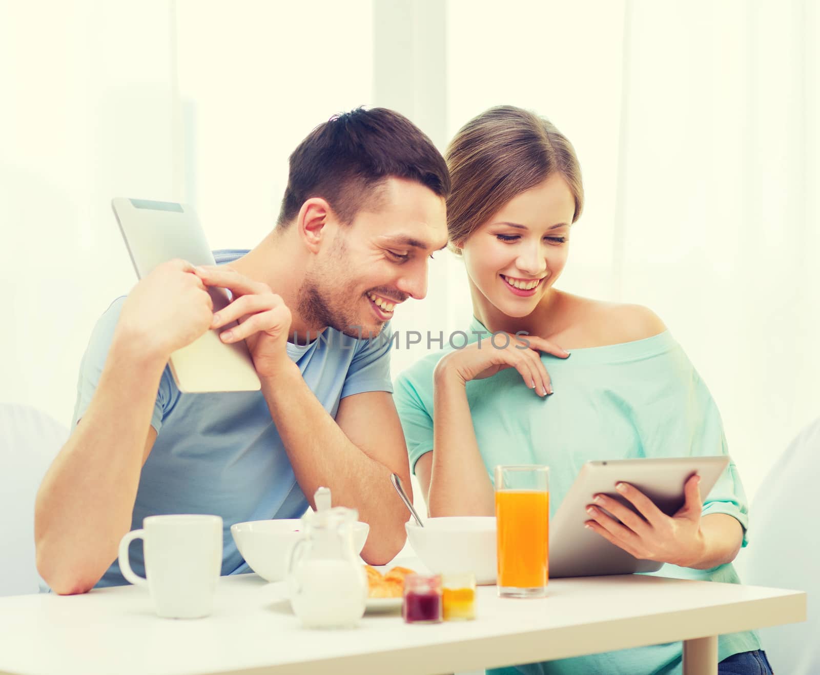 food, home, couple and technology concept - smiling couple with tablet pc reading news and having breakfast at home