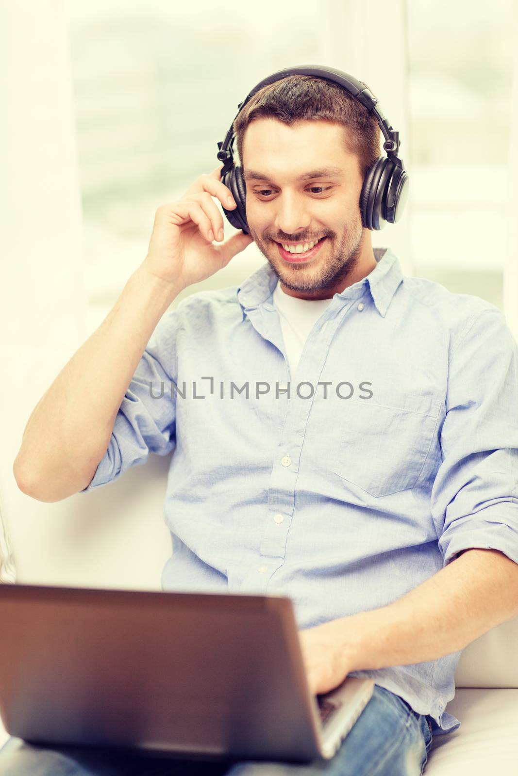 smiling man with laptop and headphones at home by dolgachov