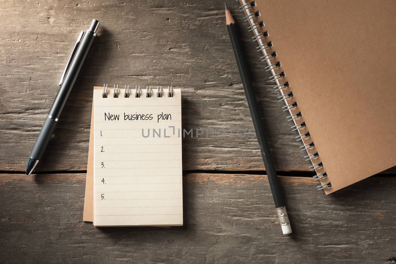 Small notepad with text, pen, and pencil on rustic wood background with low key scene.