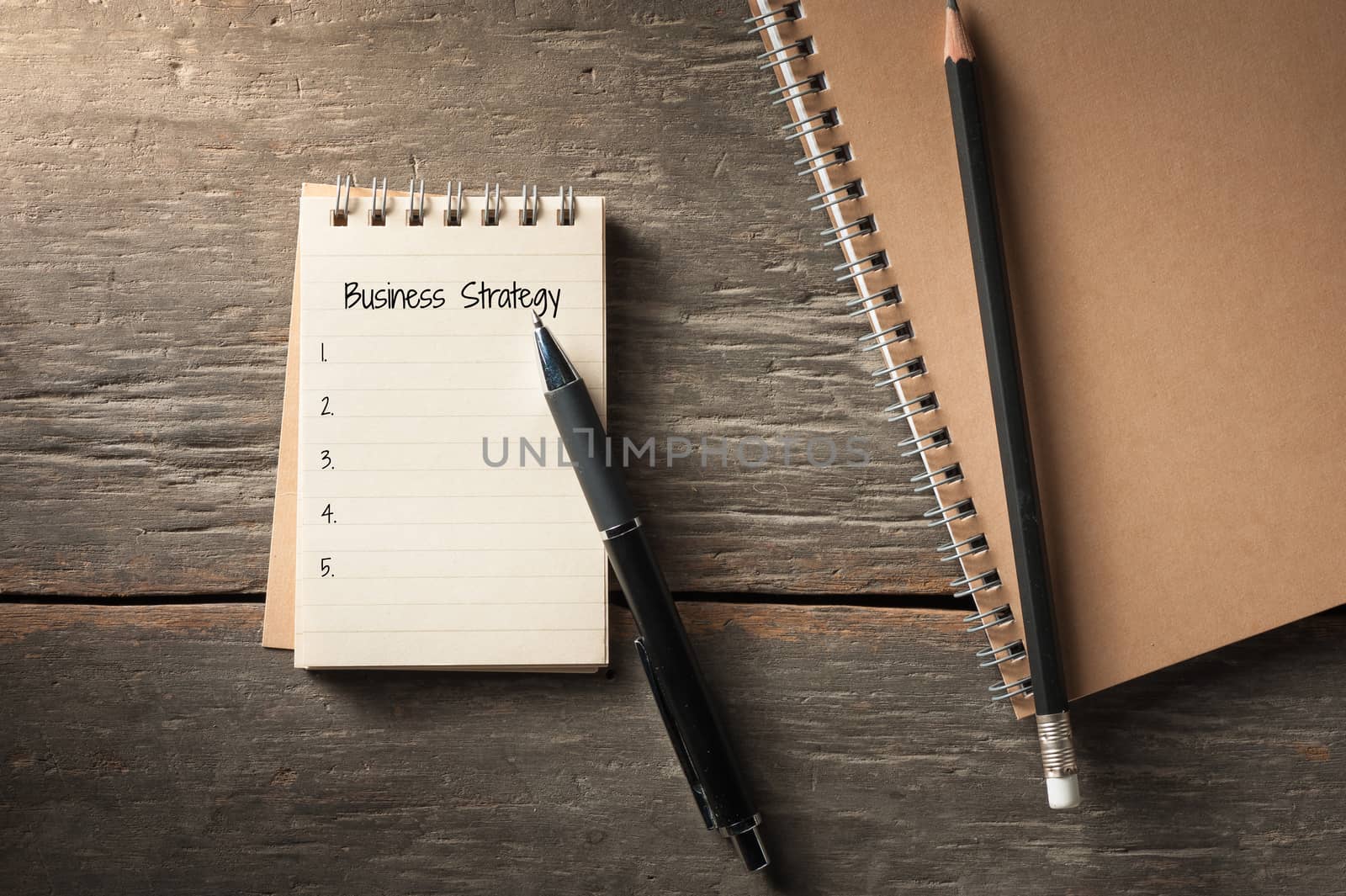 Small notepad with pen and pencil on rustic wood background with low key scene.