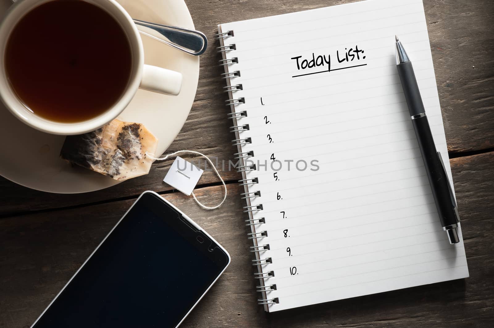 Small notepad with written messeage,  a cup of tea, pen, pencil and cellphne on rustic wood background with low key scene