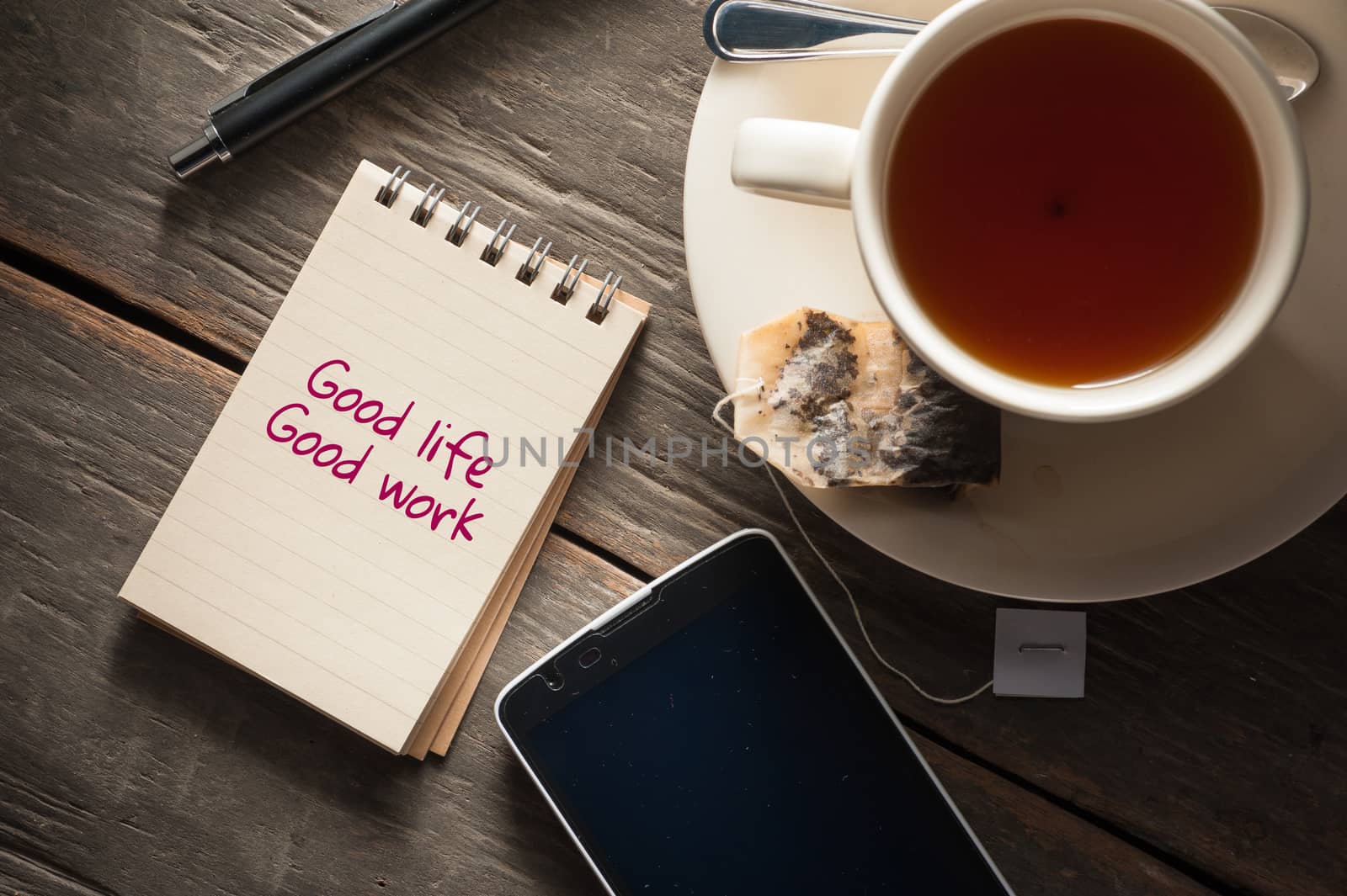 Small notepad with written messeage,  a cup of tea, pen, pencil and cellphne on rustic wood background with low key scene