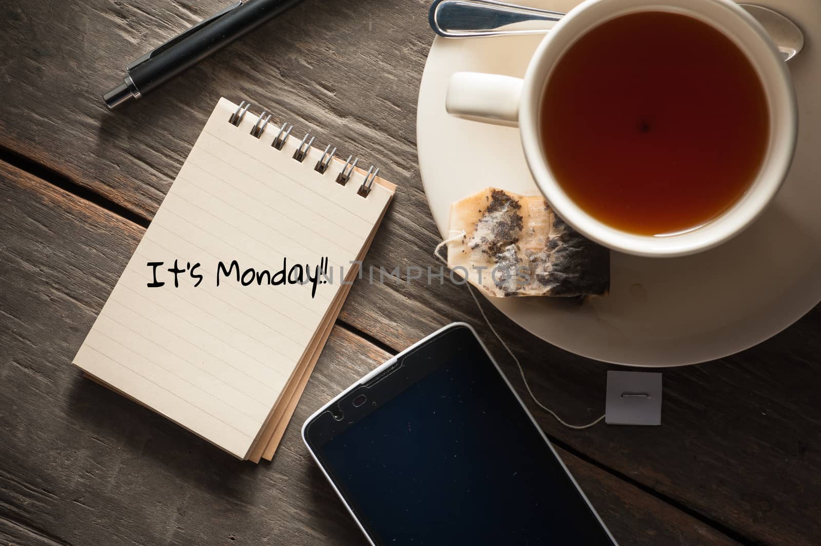 Small notepad with written messeage,  a cup of tea, pen, pencil and cellphne on rustic wood background with low key scene