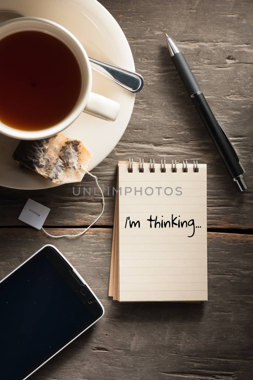 Small notepad with written words a cup of tea, pen, pencil and cellphne on rustic wood background with low key scene