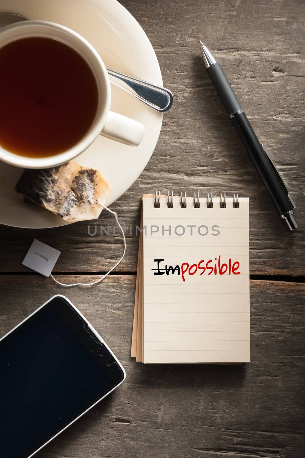 Small notepad with written words a cup of tea, pen, pencil and cellphne on rustic wood background with low key scene