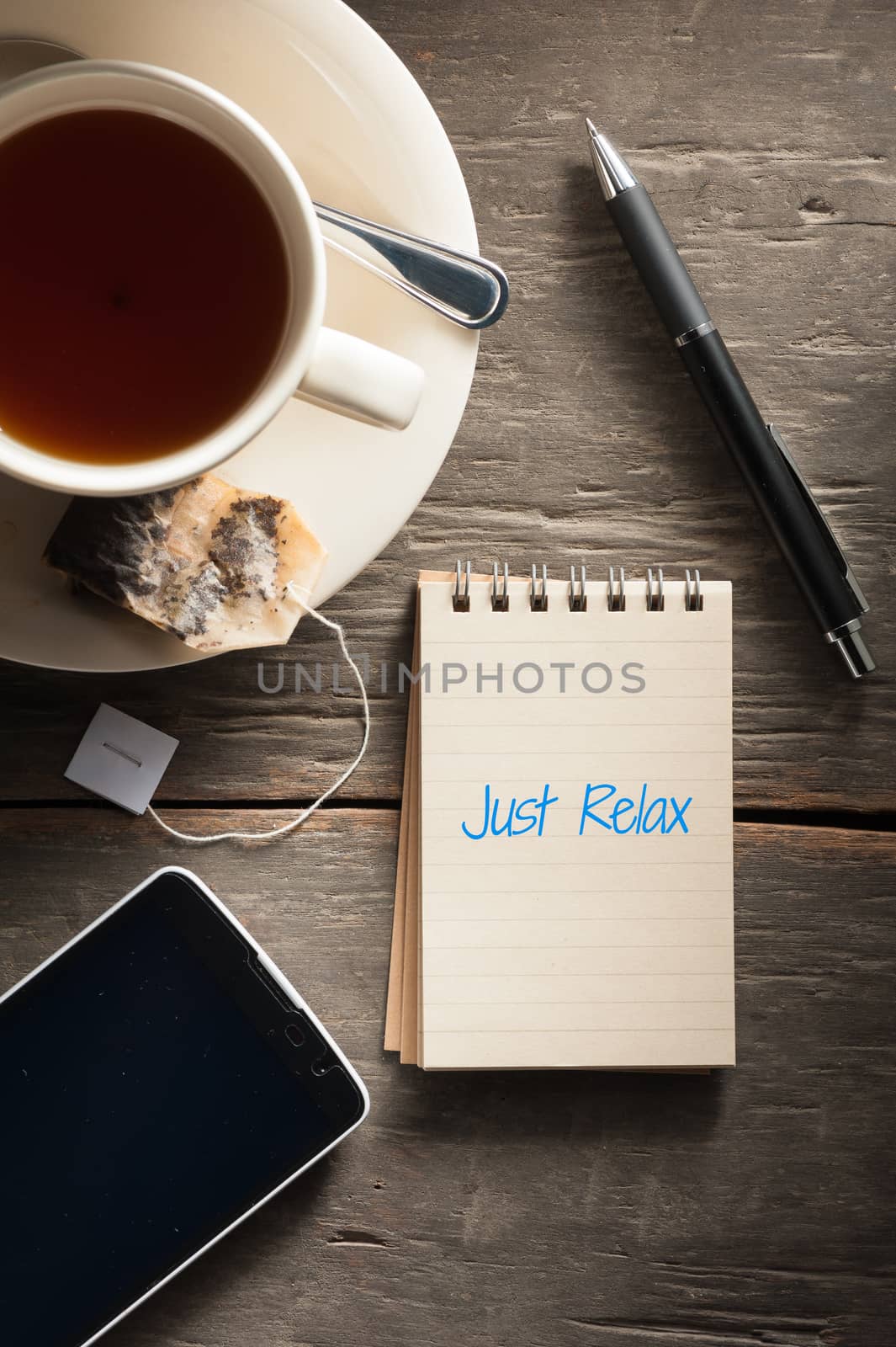 Small notepad with written words a cup of tea, pen, pencil and cellphne on rustic wood background with low key scene