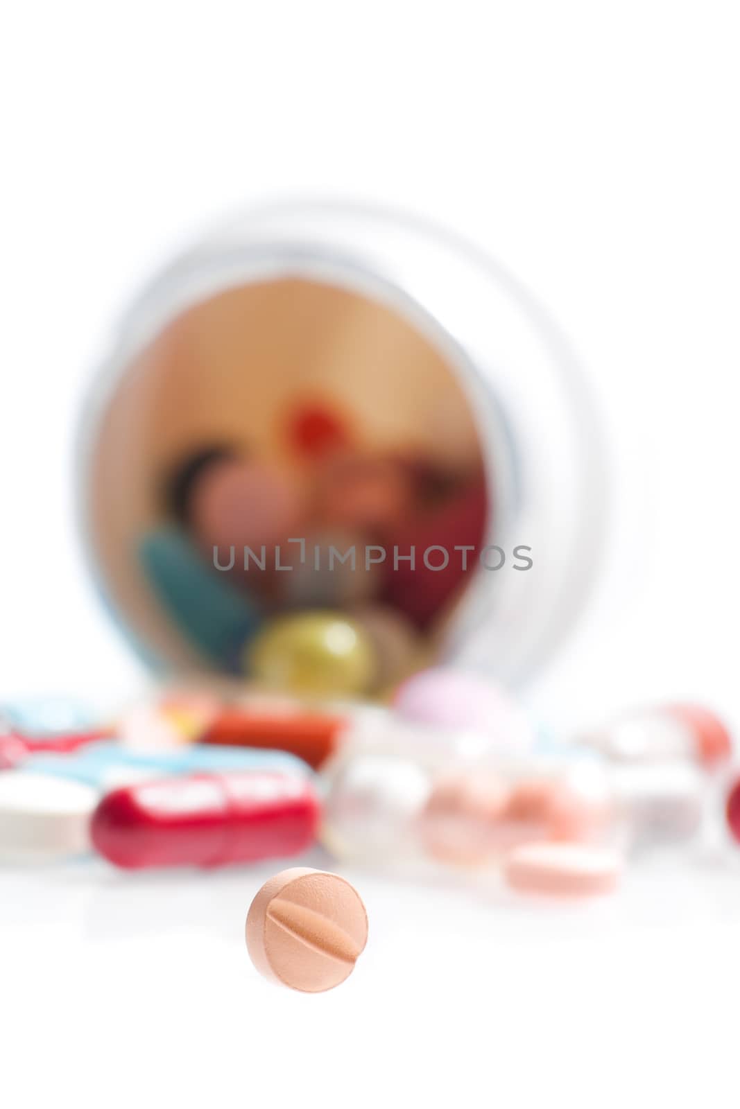 one small pill in laboratory in front of a colored pills on white table