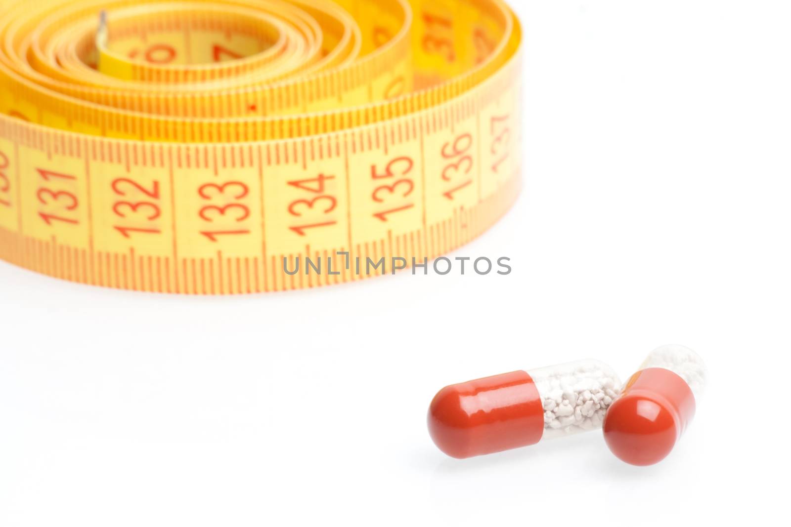 medical pills for dieting in front of measuring tape on a white background