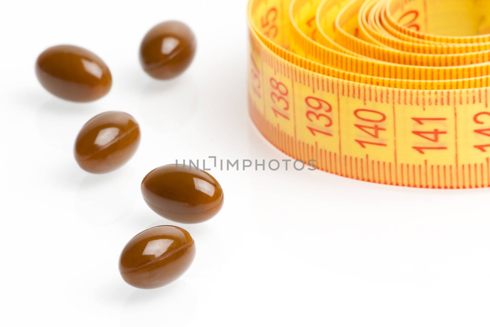 brown medical pills for dieting in front of measuring tape on a white background