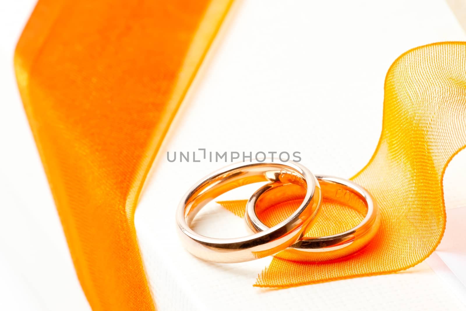 gold wedding rings near orange ribbon on white background