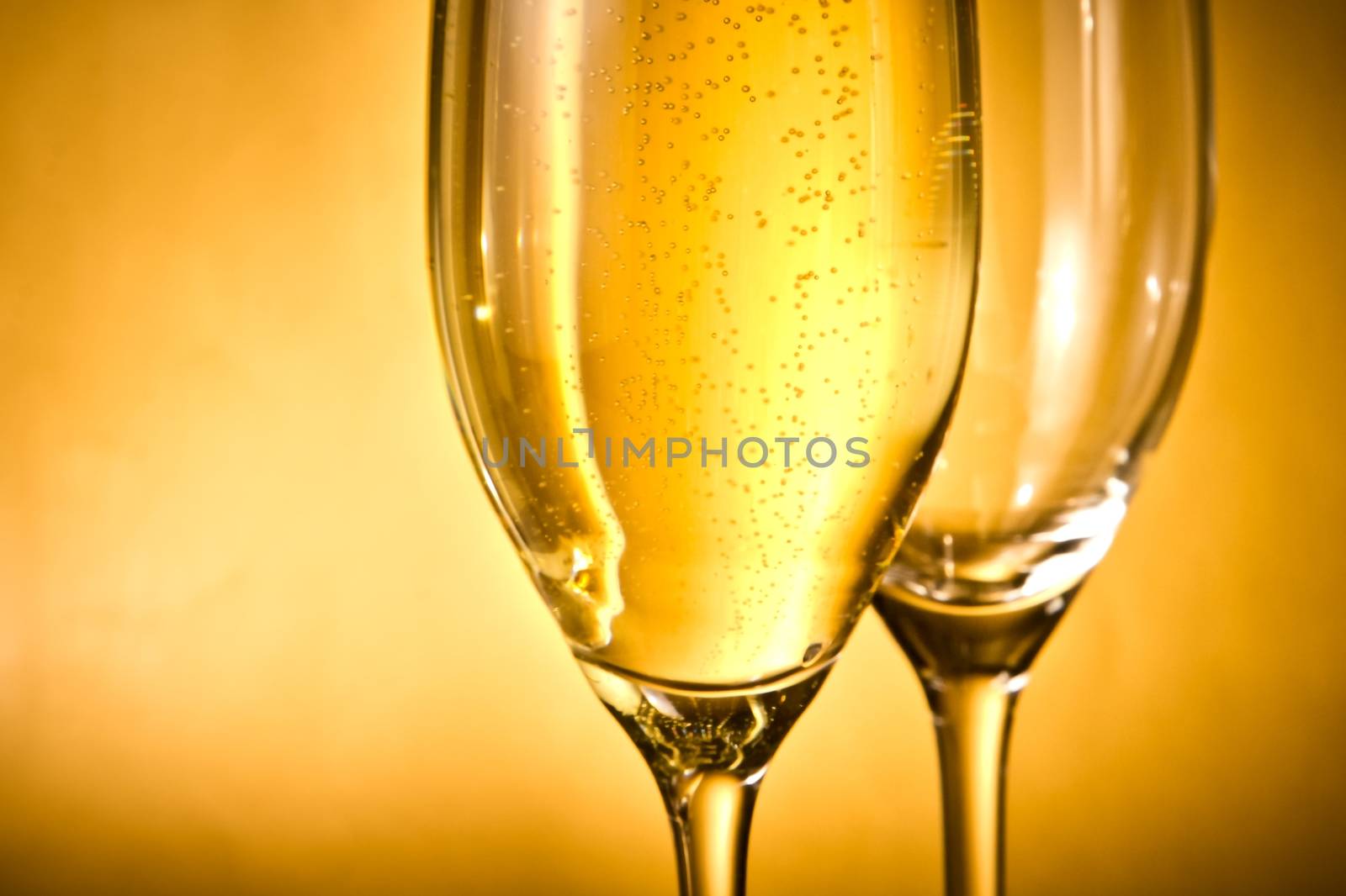 one glass of champagne and one empty with golden bubbles against golden background