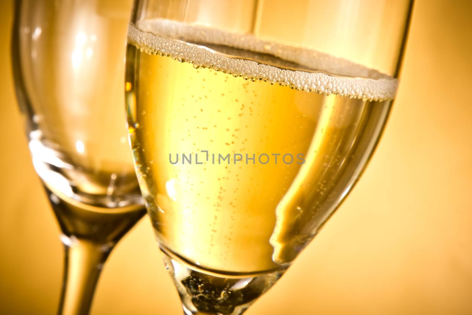 one flute of champagne and one empty with golden bubbles and space for text by donfiore