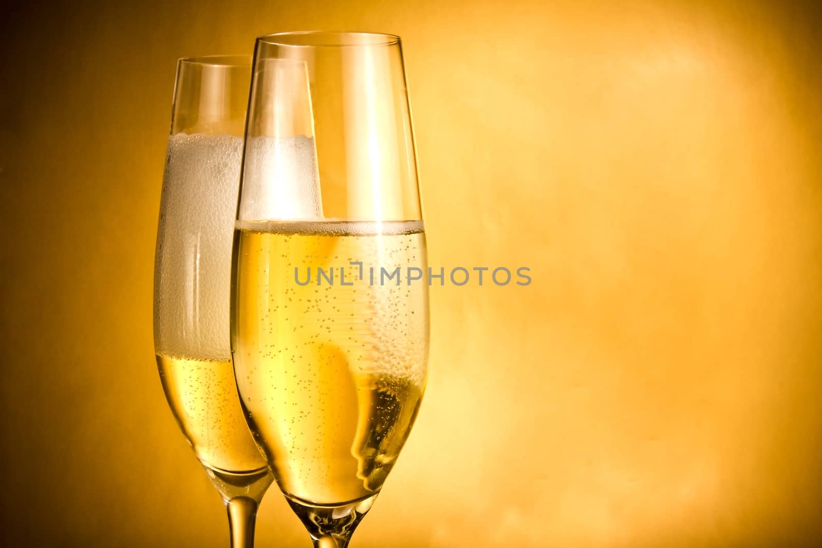 two flutes of champagne with golden bubbles and white foam by donfiore