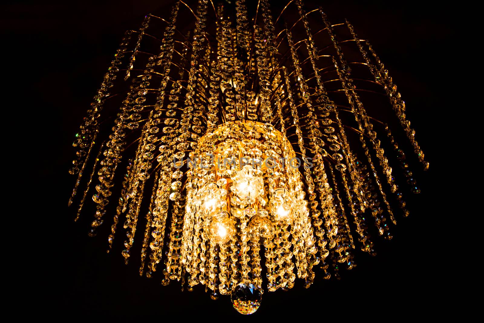 a crystal chandelier glows with golden light on dark background