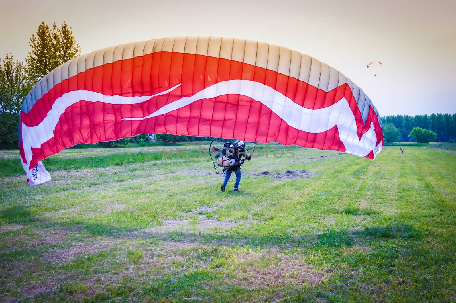 man with red motorized paraglider takes off from a green field