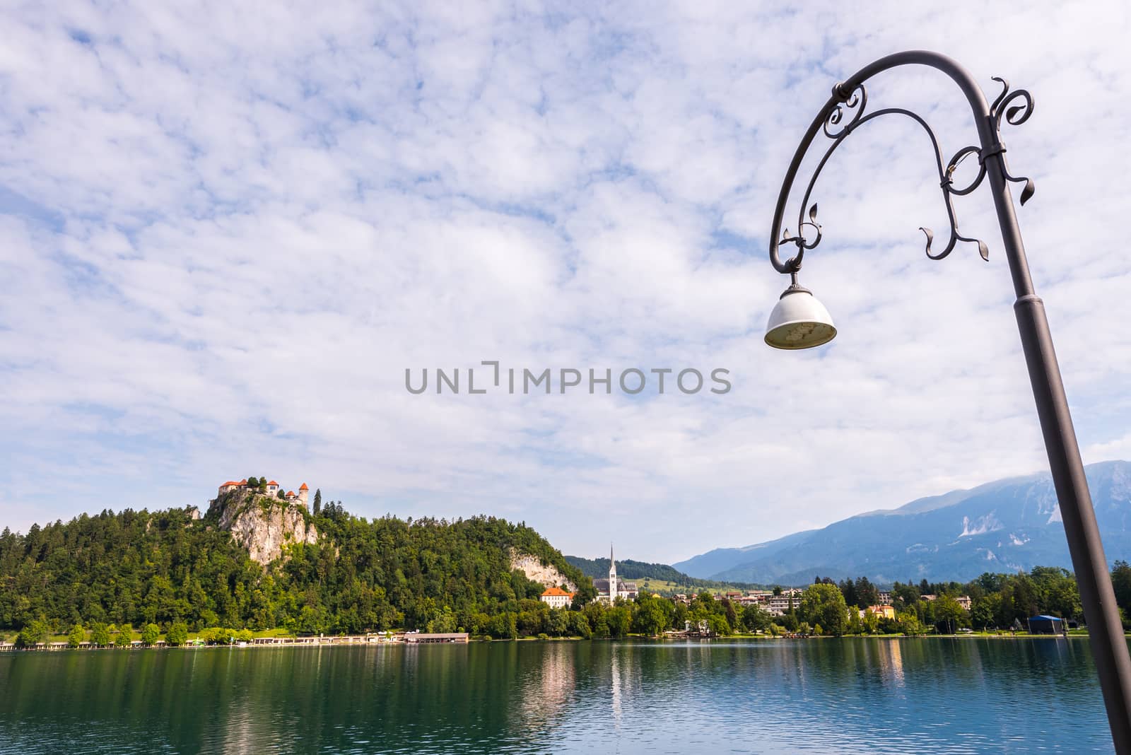 Bled Castle on a Rock at Bled Lake in Slovenia Reflected on Water Surface with Cloudy Sky and Street Lamp in Foreground
