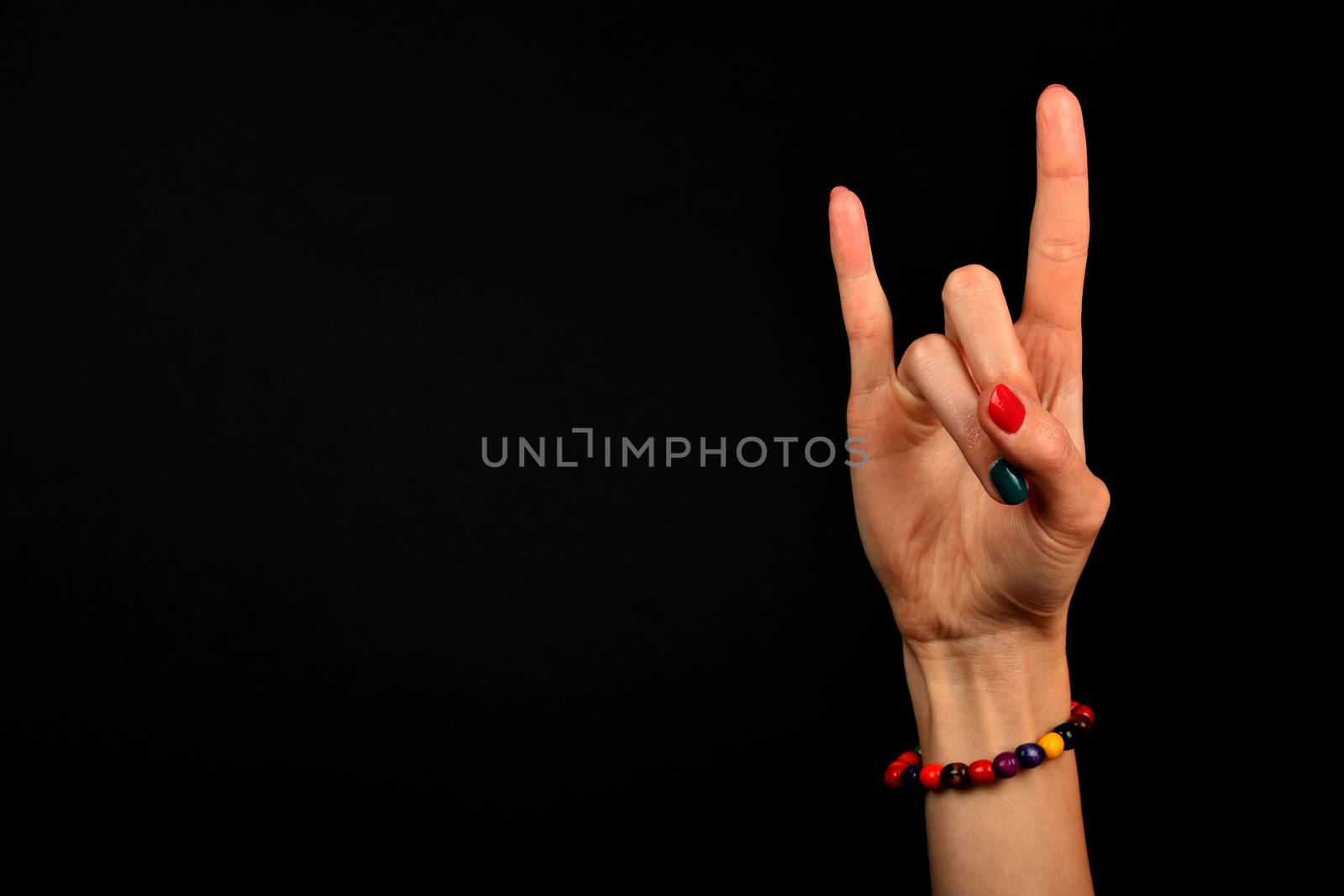 Female hand with devil horns rock metal sign symbol gesture and colorful wooden beads isolated on black background