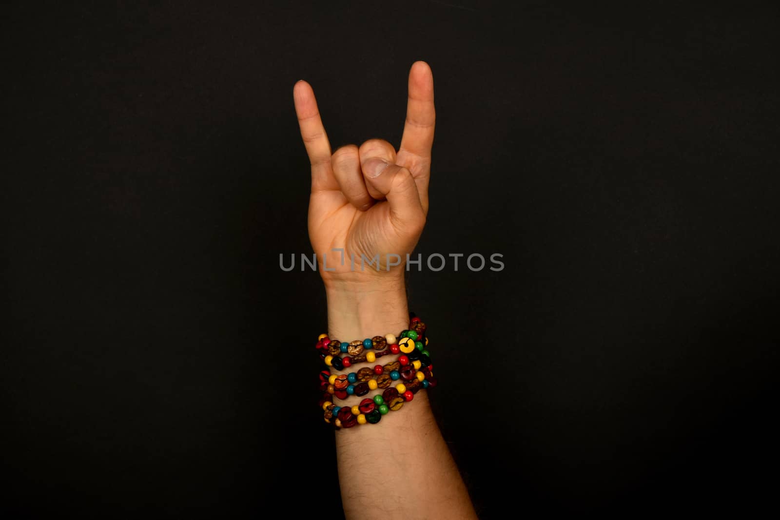 Male hand with devil horns rock metal sign symbol gesture and colorful wooden beads isolated on black background