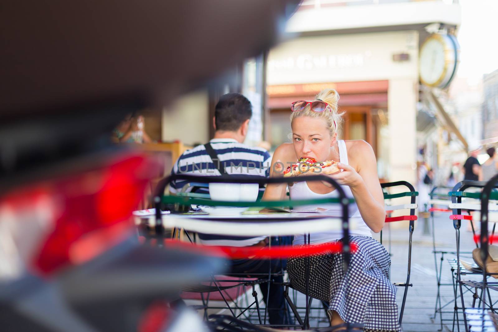 Woman eating pizza outdoor in cafeteria. by kasto